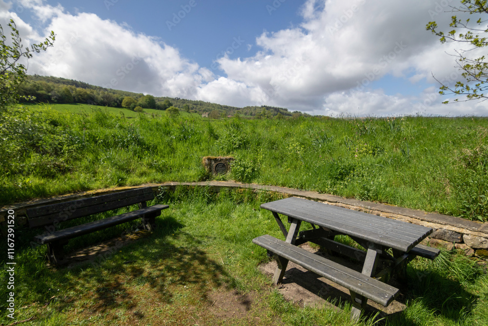 Quite a picnic area with tables and benches facing a green hillside under a brilliant, somewhat cloudless sky, Nidderdale, North Yorkshire, UK. Quite a picnic area with tables and benches facing a green hillside under a brilliant, somewhat cloudless sky, Nidderdale, North Yorkshire, UK.