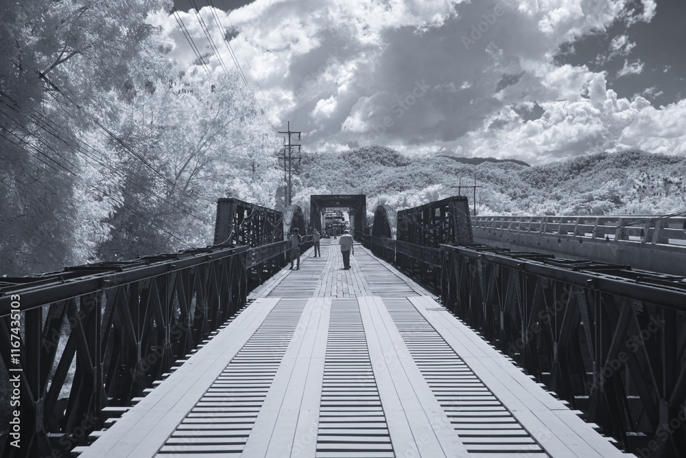 Obraz premium Infrared photography, a long, narrow bridge extending into the distance with wooden planks forming the pathway at Black bridge, Lampang, Thailand