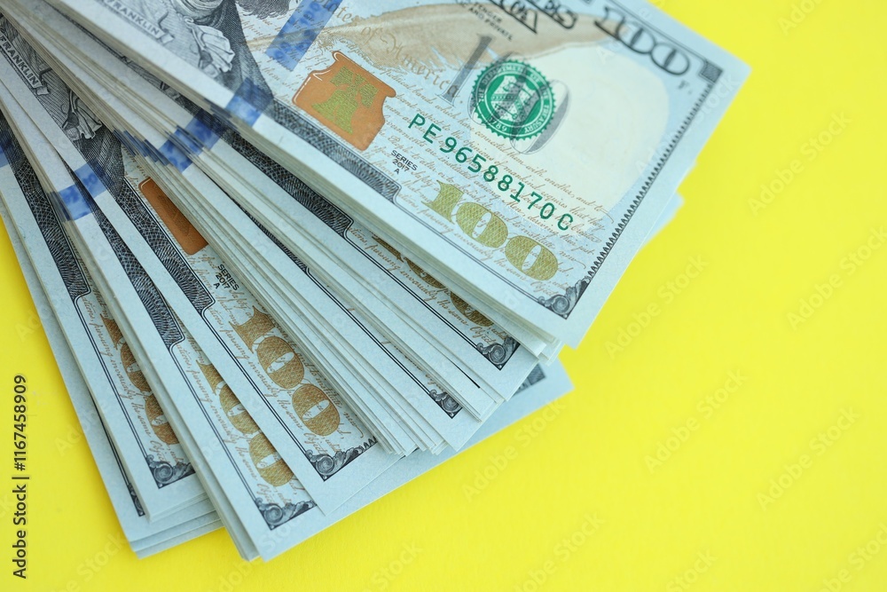 Big amount of hundred dollar bills in thick stack lies on bright yellow color paper background Big amount of hundred dollar bills in thick stack lies on bright yellow color paper background