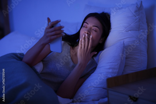 Obraz w ramie Beautiful young woman with mobile phone yawning while lying in bed at night