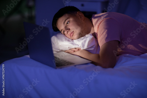 Handsome young tired man with laptop lying in bed at night