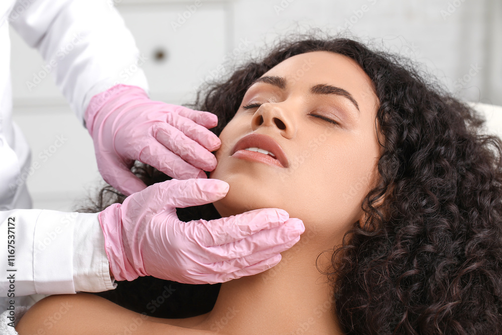 Fototapeta premium Beautiful young African-American woman receiving facial massage in beauty salon, closeup