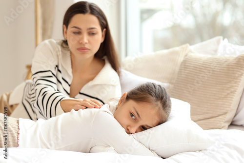 Mother apologizing to her daughter lying in bedroom photo