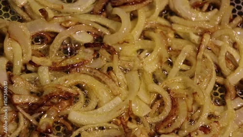 Golden crispy fried onion rings floating in hot bubbling oil, representing delicious fast food and snack indulgence, captured with a close-up view showcasing rich colors and texture.