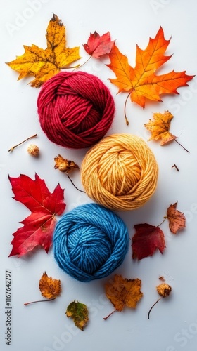 Colorful yarn balls surrounded by autumn leaves on a light background
