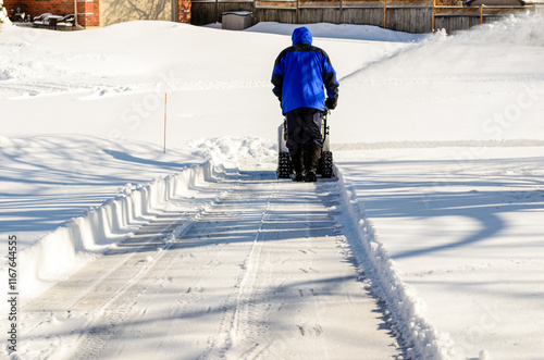 Rear view of a man using a snow blower to clear a residential driveway photo