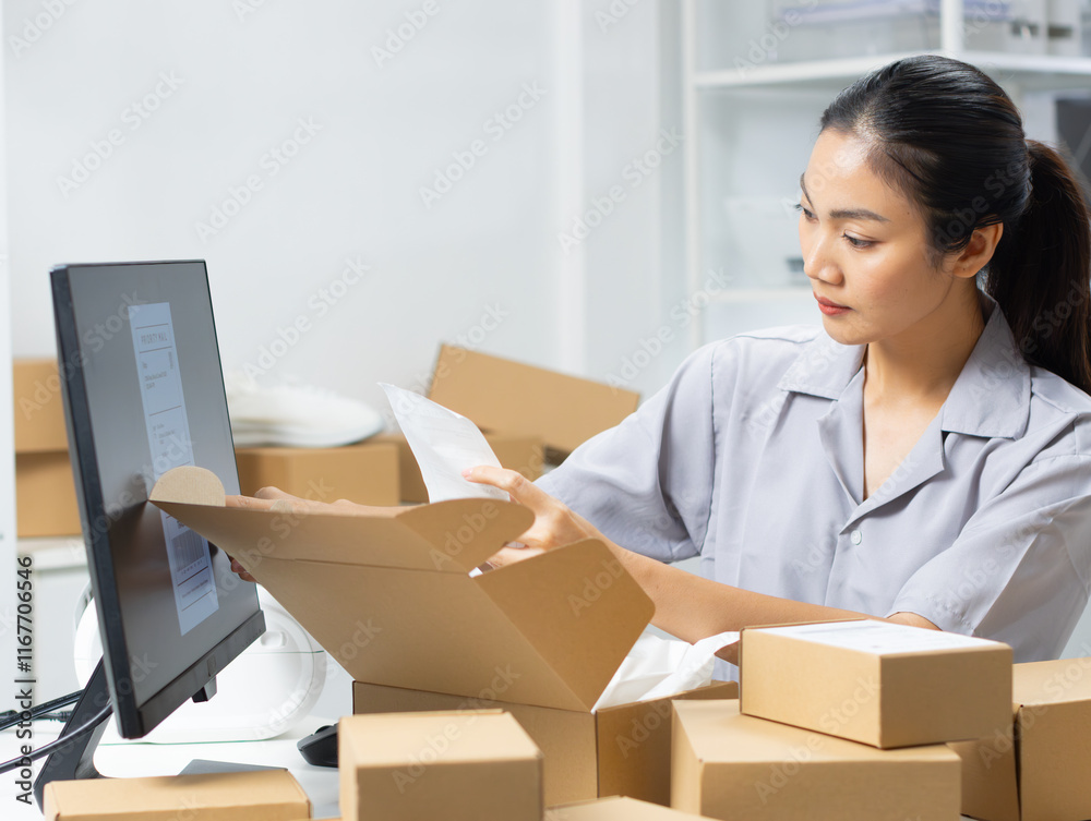 Young Asian inventory manager is preparing a package to ship, working on a computer to check order detail information at warehouse. Online store shop owner managing product for dispatch to a client. Young Asian inventory manager is preparing a package to ship, working on a computer to check order detail information at warehouse. Online store shop owner managing product for dispatch to a client.