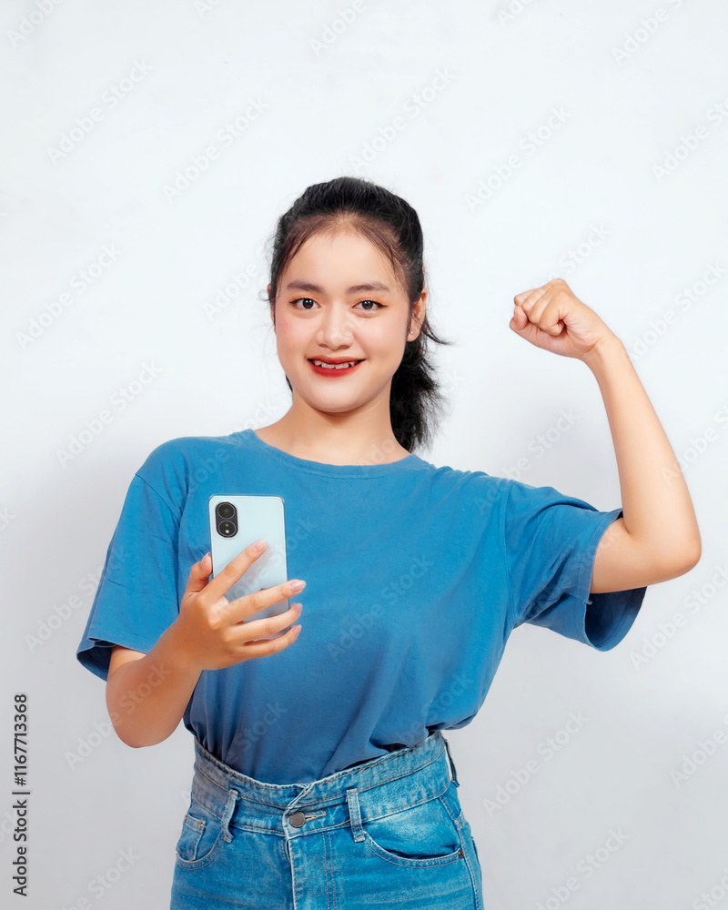 Overjoyed young Asian woman is raising her hands in the air with happy successful expression with holding phone