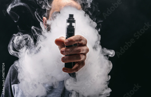 Unrecognizable man in the cloud of vape smoke. Guy smoking e-cigarette to quit tobacco. Vapor and alternative nicotine free smoking concept, copy space