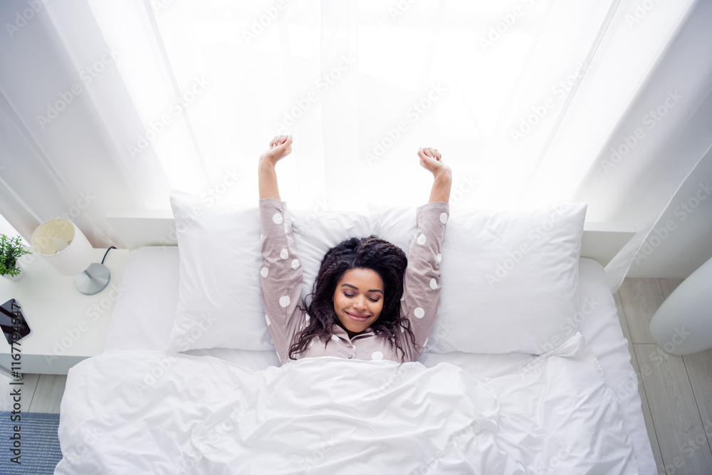 Young woman in cozy pajama waking up in bed with joyful smile in sunlit bedroom Young woman in cozy pajama waking up in bed with joyful smile in sunlit bedroom