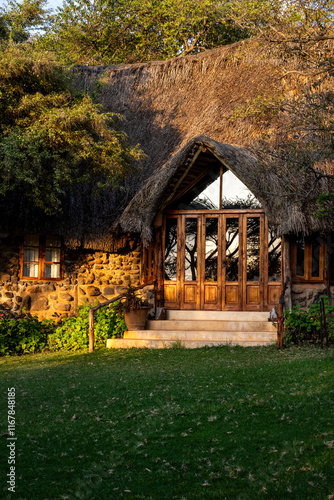 Luxury resort experience, at traditional African game lodge, welcome entrance with cement stairs, wood doors, and thatch roof in early morning sunlight, Lewa Conservancy, Kenya, Africa
