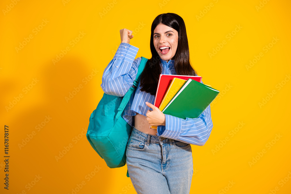 Young cheerful student with books and backpack posing against yellow background Young cheerful student with books and backpack posing against yellow background