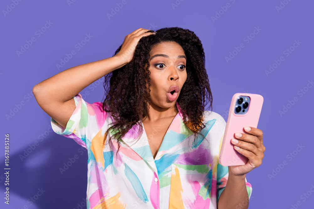 Surprised young woman looking at smartphone with mouth open, wearing colorful shirt Surprised young woman looking at smartphone with mouth open, wearing colorful shirt