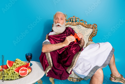 Portrait of impressed charismatic theater performer sit throne ancient god costume hold binoculars isolated on blue color background