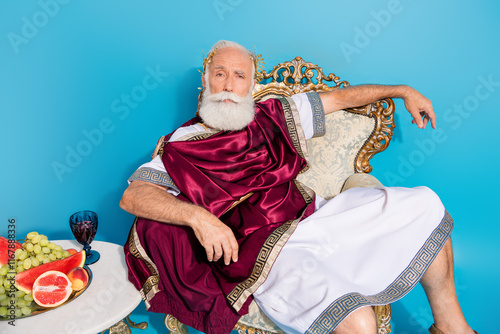 Photo of confident mythological philosopher politician sitting throne wearing traditional dress isolated on blue color background photo