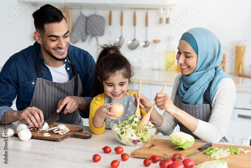 Happy islamic family with little daughter preparing food together in kitchen, middle eastern parents and cute female child making healthy salad for breakfast or lunch, enjoying cooking at home photo