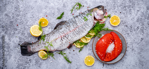 Gutted and cleaned raw trout and fresh red caviar with lemon, dill, salt and spices on gray table background, top view photo