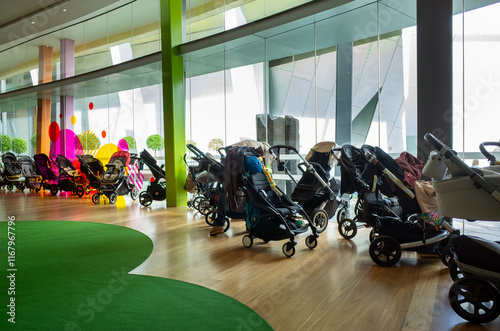 A variety of baby strollers are parked indoors in a family-friendly space with carpeted floors and large windows, concept of pram parking in places such as libraries, museums, play centers. photo