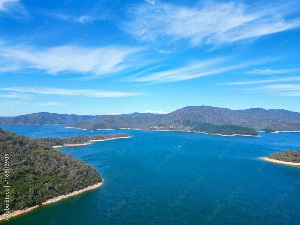 A stunning aerial view of Lake Eildon, Australia, captured by a drone. The vibrant blue water, lush green islands, and surrounding hills create a serene and picturesque landscape under a clear sky A stunning aerial view of Lake Eildon, Australia, captured by a drone. The vibrant blue water, lush green islands, and surrounding hills create a serene and picturesque landscape under a clear sky
