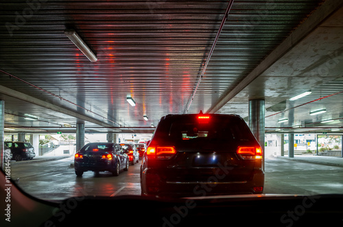 A perspective view from inside a car, looking out at a line of vehicles waiting to exit an underground car park in a shopping center. The red brake lights dimly lit the concrete ceiling. photo