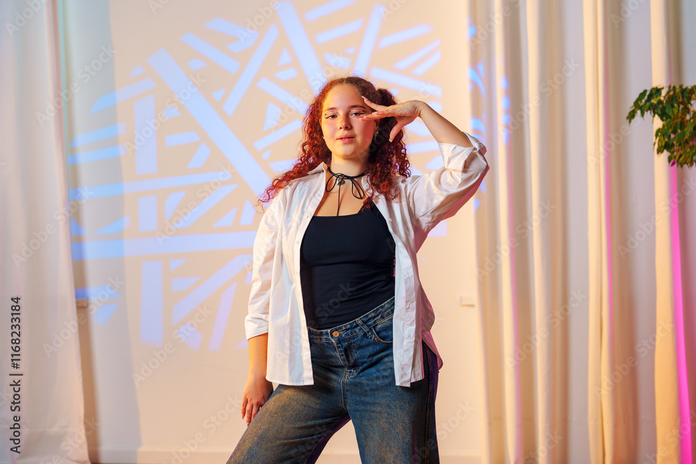Fototapeta premium A young woman with curly red hair poses in front of a patterned background