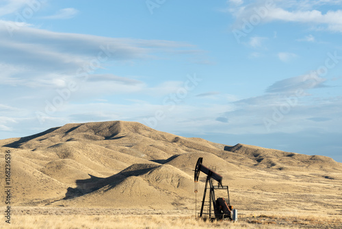 Single working oil rig in a plains area of Texas Oklahoma New Mexico or North Dakota in the unpopulated countryside pumping for production of fossil fuel with rolling hills in the distance photo