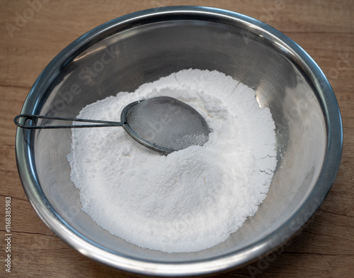 Sifted white powdered sugar in a stainless steel bowl prepared as an ingredient for baking cakes, gingerbread, or for preparing sweet dishes.
