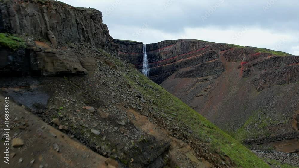 Aerial reveal shot of Hengifoss Waterfall cascading over layered basalt cliffs in East Iceland. The camera reveals the stunning geological patterns and rugged terrain. Aerial reveal shot of Hengifoss Waterfall cascading over layered basalt cliffs in East Iceland. The camera reveals the stunning geological patterns and rugged terrain.