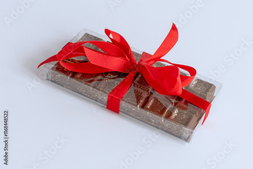 Hand made trend dessert Dubai chocolate lies packaged in transparent plastic papaer with red ribbon on white background photo