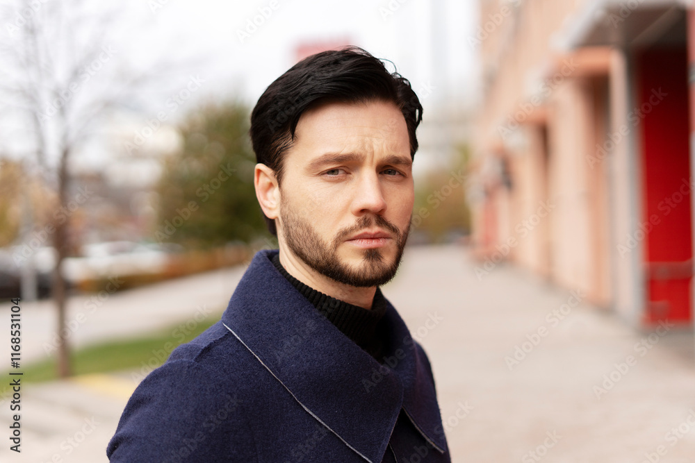 Fototapeta premium Attractive bearded young man in stylish clothes posing at camera on the street in the city