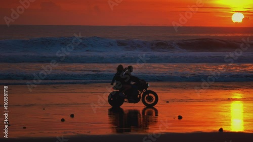 Man, woman ride vintage motorcycle or motorbike along ocean coast in Bali. Couple sits and riding on a scooter on sandy sea beach, sunset. Travelers enjoy journey on bike, love on adventure, road trip