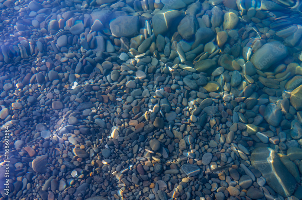 Underwater pebble backgrounds. Colorful stones sea bottom in the sun rays. View from above through clear water. Seascape wallpaper texture. Defocus.