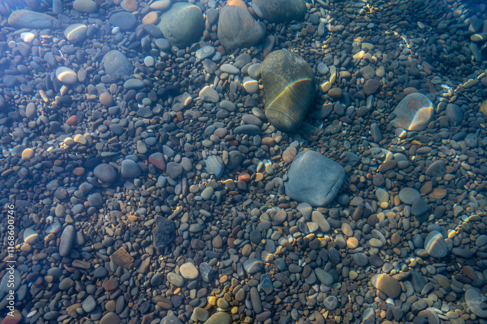 Underwater pebble backgrounds. Colorful stones sea bottom in the sun rays. View from above through clear water. Seascape wallpaper texture. Defocus.