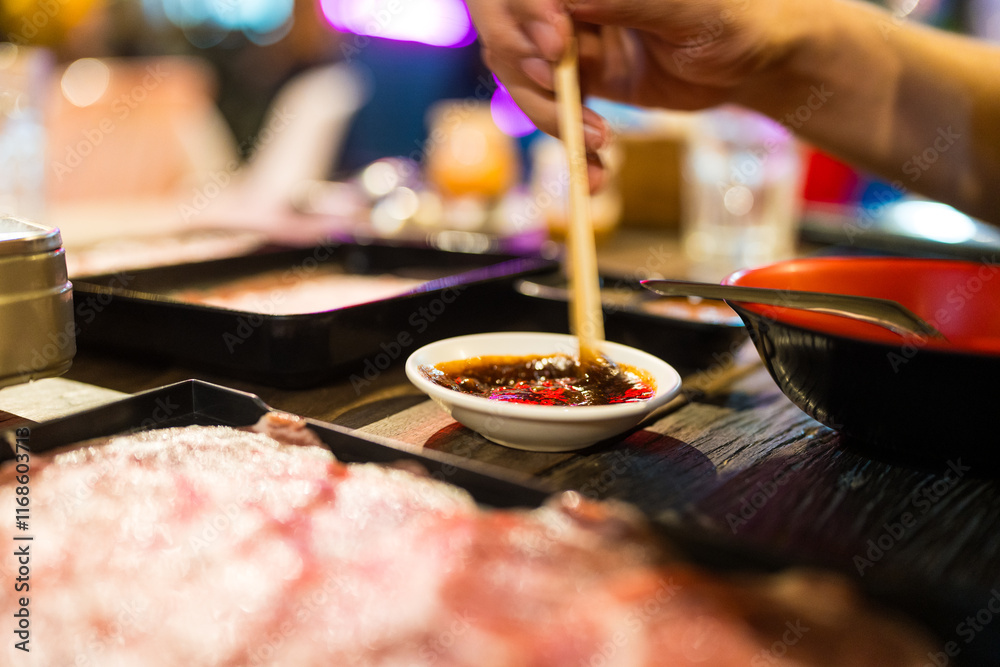 Fototapeta premium Hand man uses wood chopsticks mix and stir the dipping sauce for eating Thai style local hot pot in outdoors restaurant