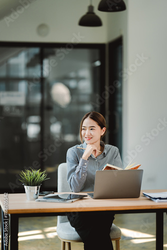 Beautiful Asian female student studying online and taking notes Female accountant makes annual financial and tax reports.