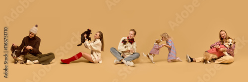 Photography Cheerful group of people posing with their dogs, all dressed in warm, stylish winter outfits against a beige background