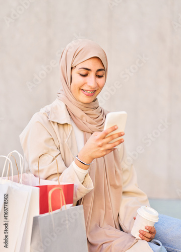 Smiling arab woman wearing hijab using smartphone after shopping