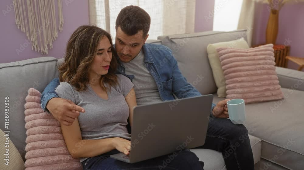 Couple sitting together on a couch at home looking at a laptop with the man holding a cup Couple sitting together on a couch at home looking at a laptop with the man holding a cup