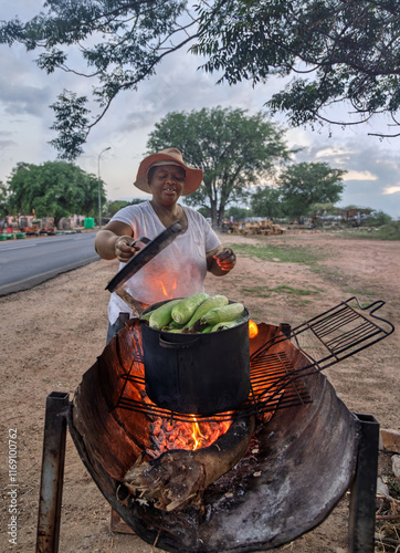 African street vendor, woman selling boiled corn on the fire on the side of the road in the village township