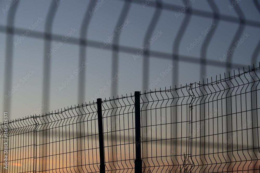 Obraz premium Barbed wire net Fence Sunset against blue sundown sky background. sunset behind the wires. Mesh Steel and Barbed Wire, Sunset with Red and blue heaven.
