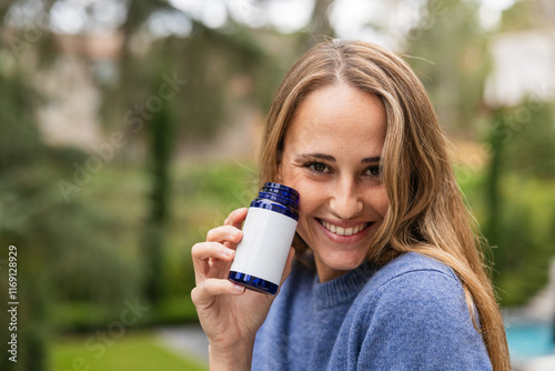 Woman smiling and holding a pill blue bottle with blank label, with empty space photo