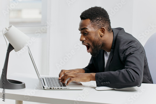 Shocked businessman in suit reacting to unexpected news on laptop while sitting at office desk photo