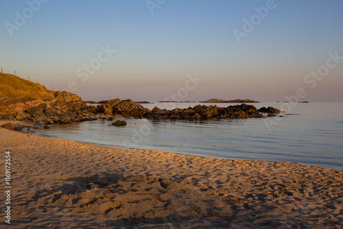 Serene beach at sunset with calm waters and rocky coastline in the background. photo