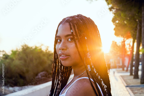 Portrait of a beautiful latin woman with braids smiling on the street with the sunset behind her