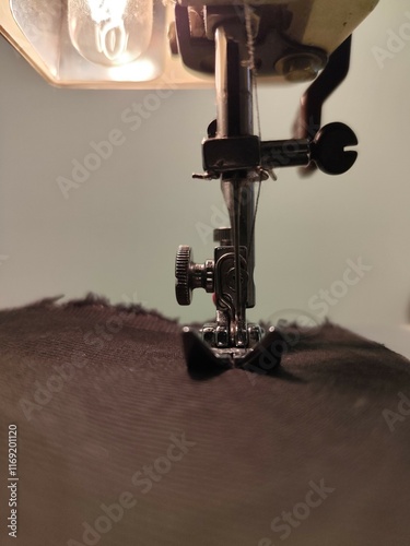 Close-up of a sewing machine focusing on the needle and presser foot working on dark fabric. The scene highlights precision, craftsmanship, and the intricate details of sewing in action.

