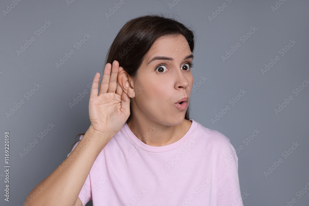 Woman showing hand to ear gesture on grey background Woman showing hand to ear gesture on grey background