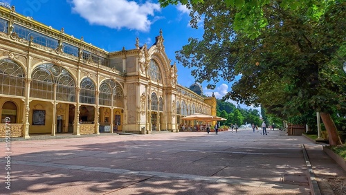 The Maxim Gorky Colonnade in Mariánske Lazne, Czech Republic with ornate architecture, large arched windows, and intricate details, surrounded by greenery and a bright blue sky.