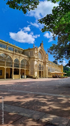 The Maxim Gorky Colonnade in Mariánske Lazne, Czech Republic, with ornate details, arched windows, and classical architecture, surrounded by greenery under a blue sky.
