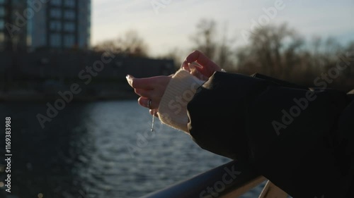 a girl with long nails on her hands stands on the river bank on a sunny day.
The glare of the sun on the water and women's hands in a warm sweater.
A girl strokes her hands while standing on the emban photo