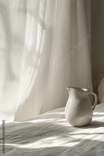 Soft morning light illuminates a ceramic pitcher on a bed with white sheets a...
